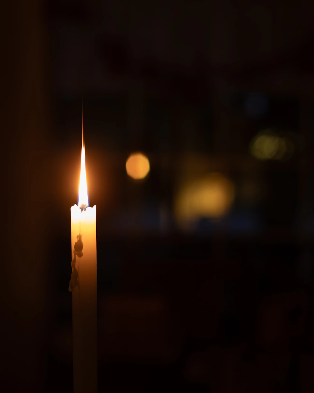 Vela encendida con luz cálida sobre un fondo oscuro desenfocado